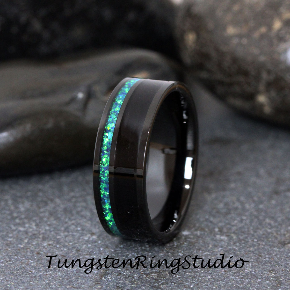 May include: A black tungsten carbide ring with a green opal inlay. The ring has a beveled edge and a polished finish.