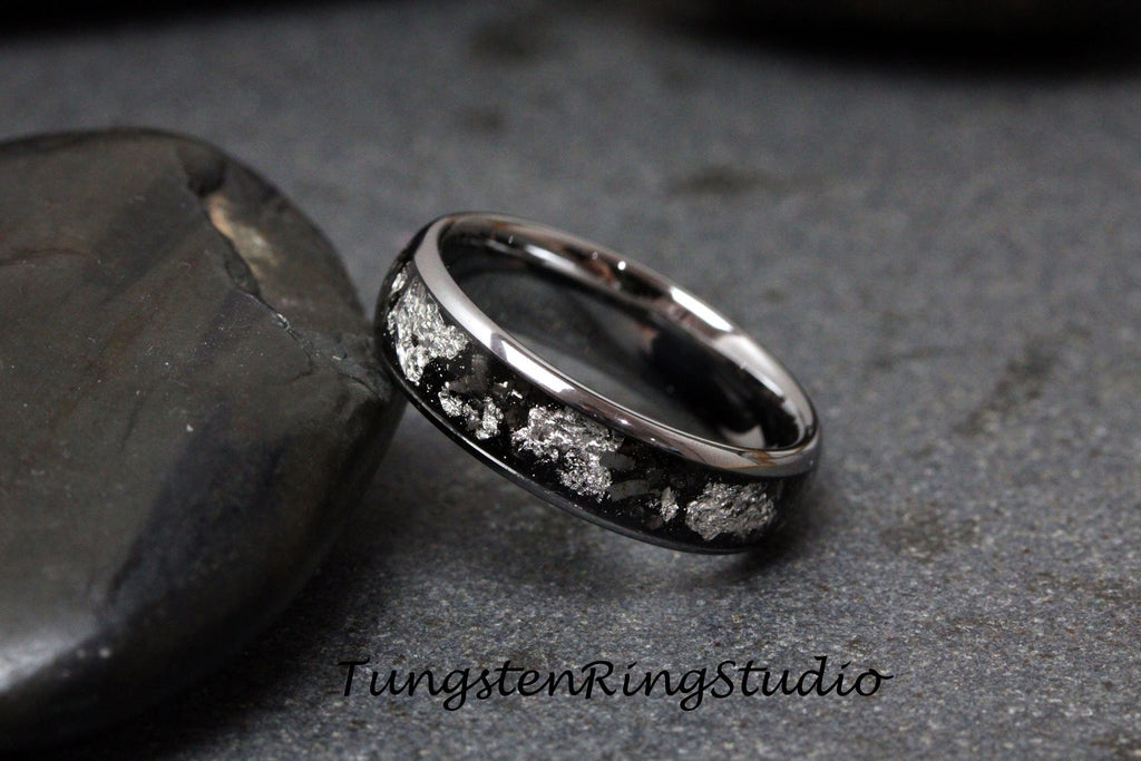 May include: A silver tungsten carbide ring with a black inlay and a silver pattern. The ring is on a gray background.