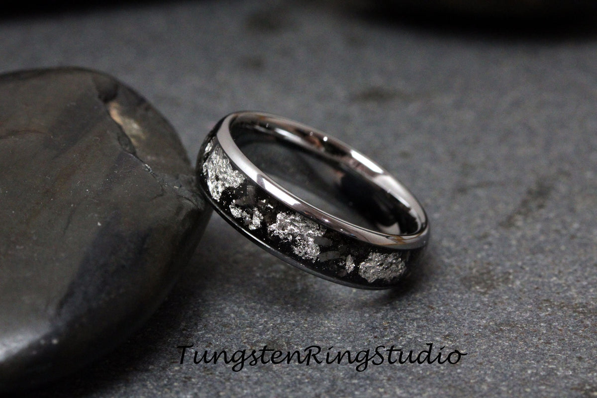 May include: A silver tungsten carbide ring with a black inlay and a silver pattern. The ring is on a gray background.