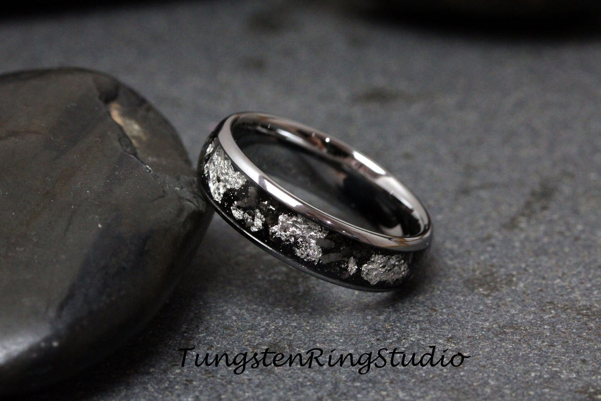 May include: A silver tungsten carbide ring with a black inlay and a silver pattern. The ring is on a gray background.