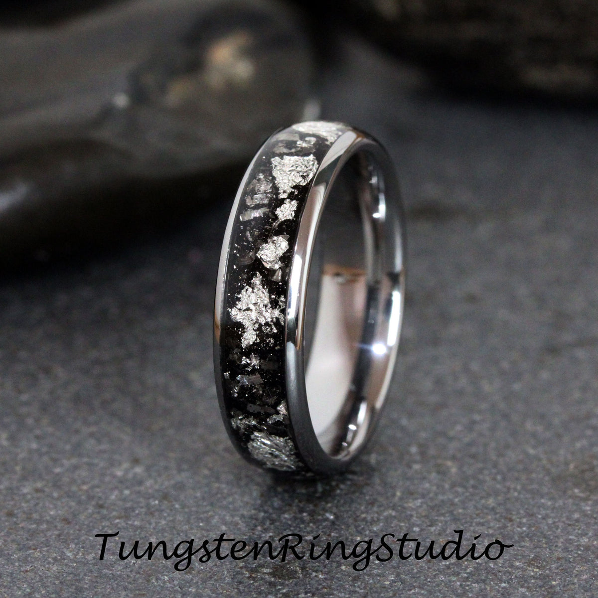 May include: A silver tungsten carbide ring with a black inlay and silver flecks. The ring is polished and has a smooth finish.