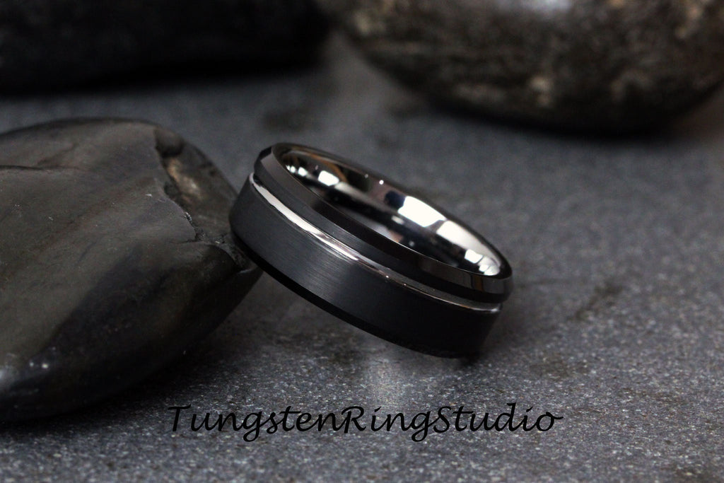 May include: A black tungsten carbide ring with a silver beveled edge. The ring has a brushed finish.