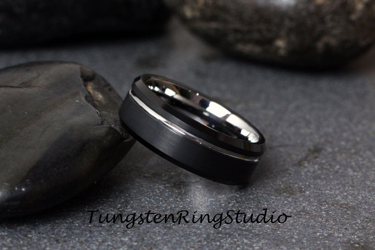 May include: A black tungsten carbide ring with a silver beveled edge. The ring has a brushed finish.