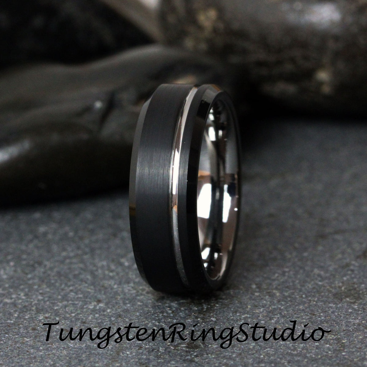 May include: A black tungsten carbide ring with a silver band around the center. The ring has a brushed finish.