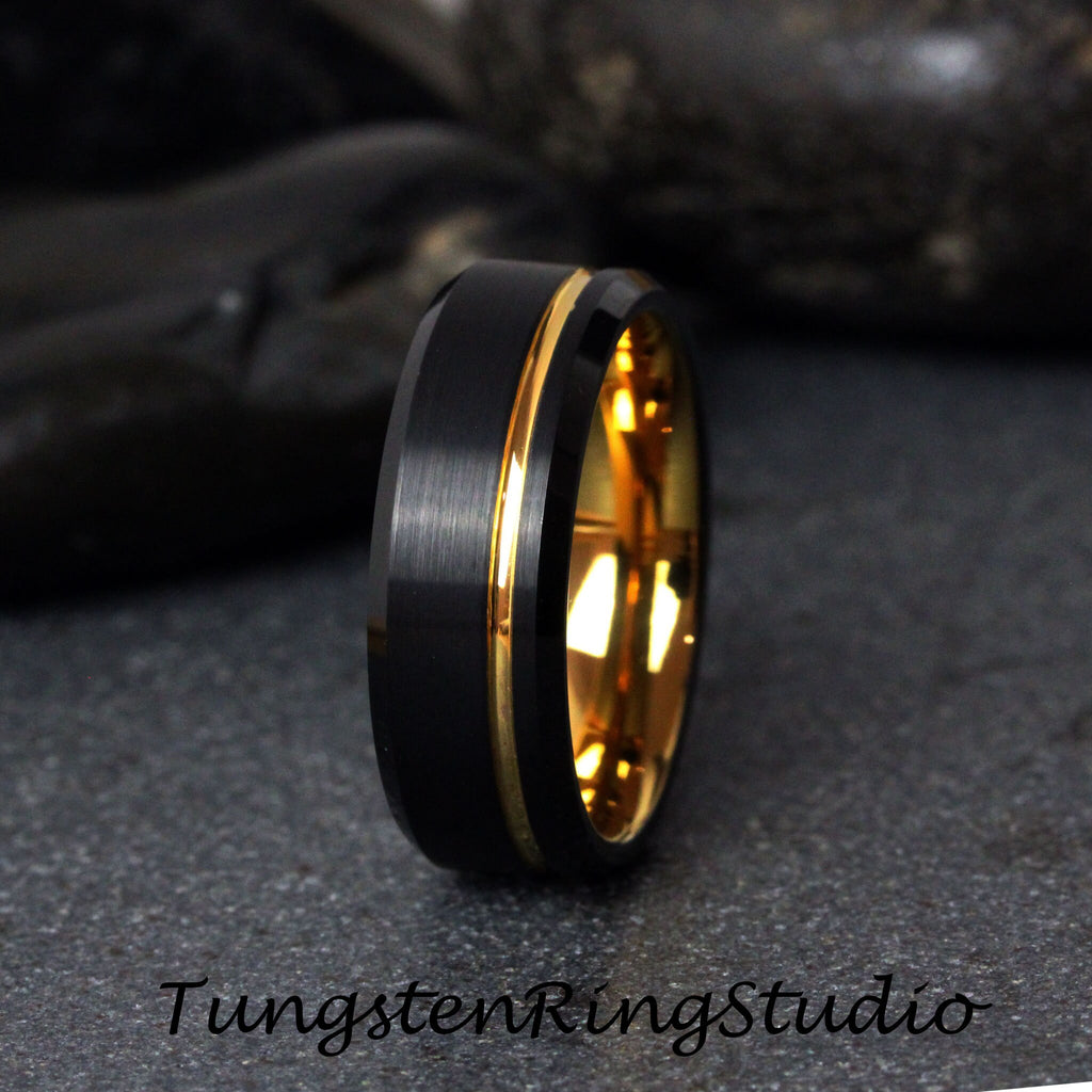 May include: A black tungsten carbide ring with a gold band. The ring has a brushed finish and a beveled edge.