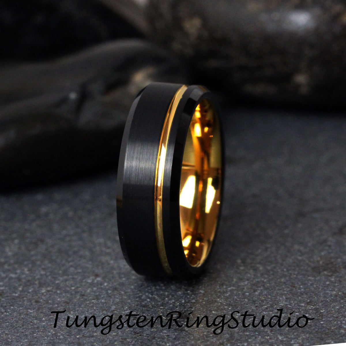 May include: A black tungsten carbide ring with a gold band. The ring has a brushed finish and a beveled edge.