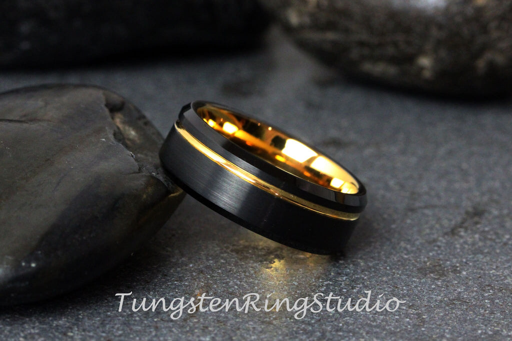 May include: A black tungsten carbide ring with a gold inlay. The ring has a brushed finish and a beveled edge.