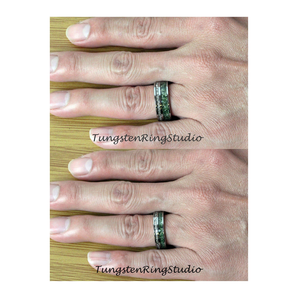 May include: A black tungsten ring with a green and black inlay. The ring is shown on a hand wearing the ring on the ring finger.