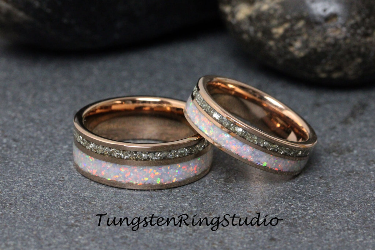 May include: Two rose gold tungsten carbide wedding bands with a white opal inlay and a row of small diamonds. The bands are on a gray textured surface.