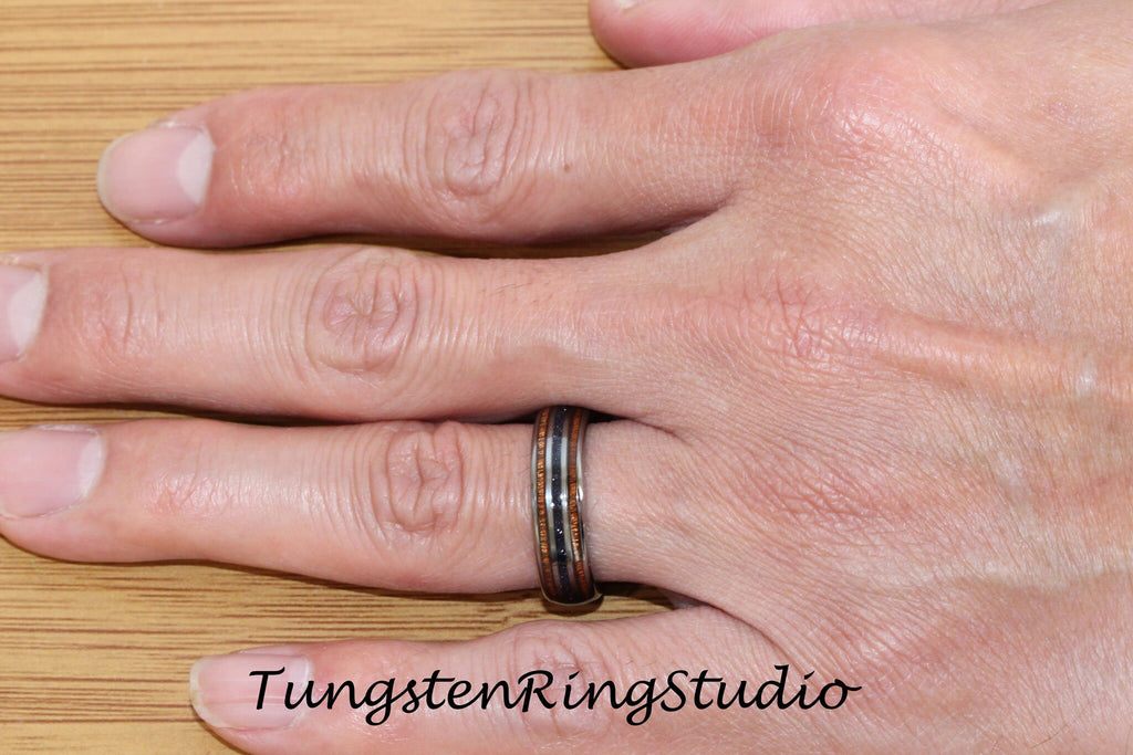 May include: A tungsten ring with a black, brown, and silver inlay. The ring is worn on a person's finger.