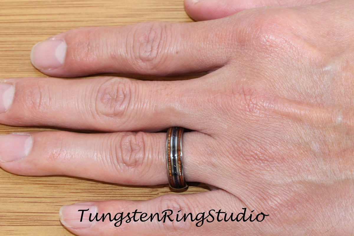 May include: A tungsten ring with a black, brown, and silver inlay. The ring is worn on a person's finger.