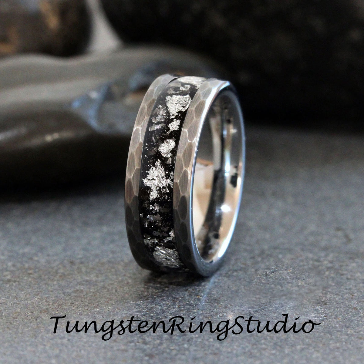 May include: A silver and black tungsten carbide ring with a hammered finish and a silver inlay. The ring has a black background with silver flecks.