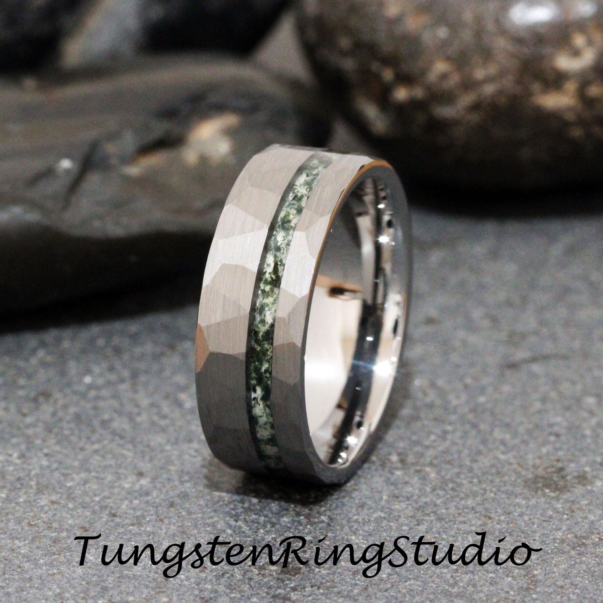 May include: A silver tungsten ring with a hammered finish and a green stone inlay. Tungsten Ring Studio is printed below the ring.