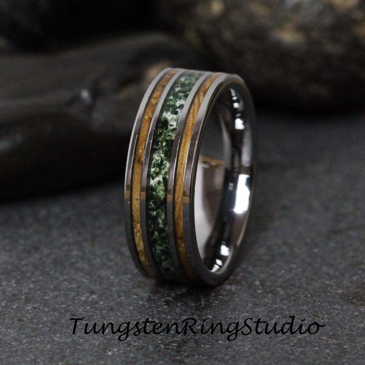 May include: A tungsten carbide ring with a green and brown wood inlay. The ring is polished and has a beveled edge.