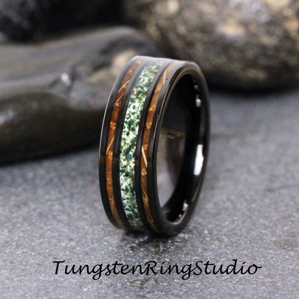 May include: A black tungsten ring with a green and brown inlay. The inlay has a wood grain pattern and a speckled green material.