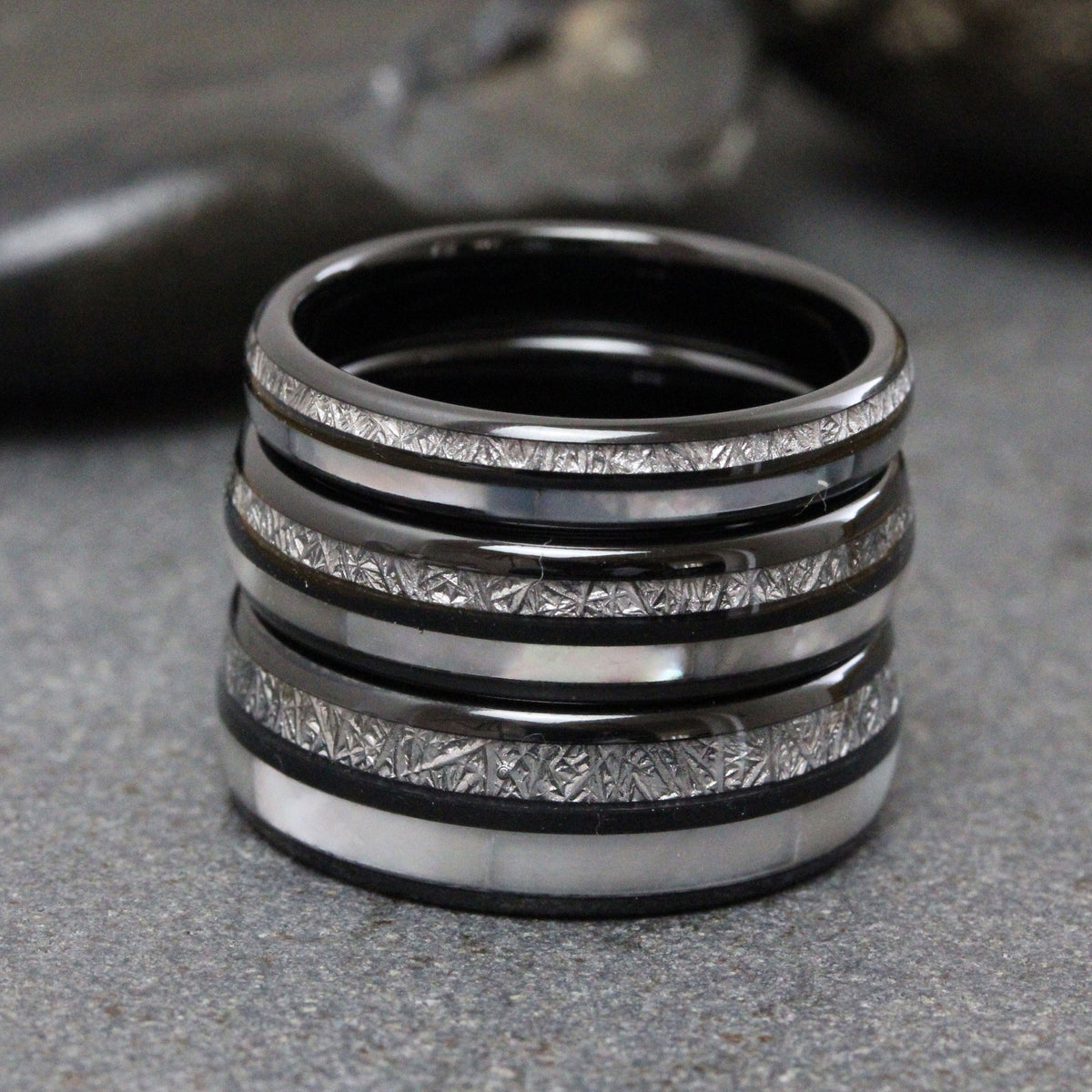 May include: Four black rings with a white inlay. The rings have a textured surface and are stacked on top of each other.