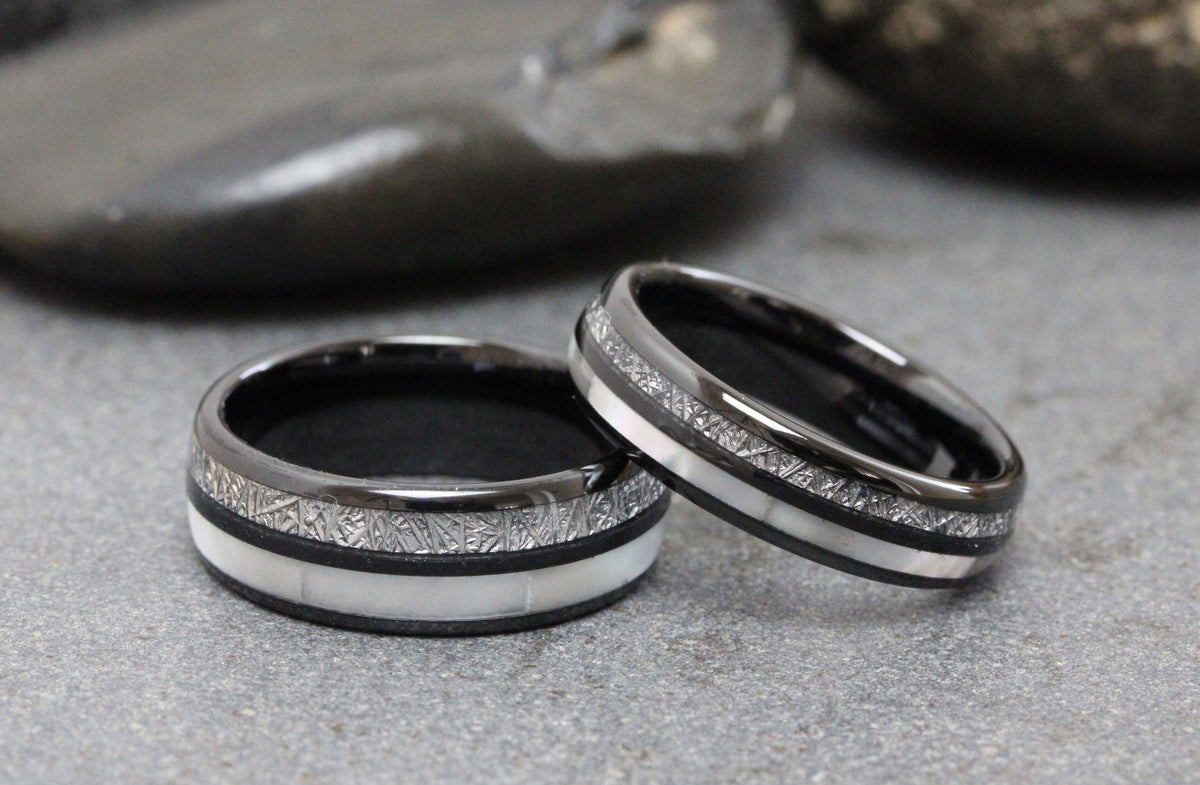 May include: Two black tungsten carbide wedding bands with a white inlay and a meteorite pattern.