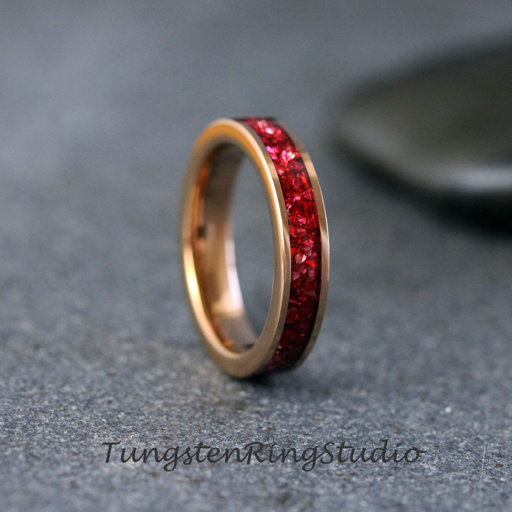May include: A rose gold tungsten carbide ring with a band of red cubic zirconia stones.