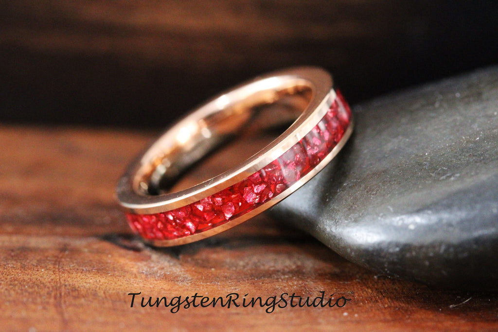 May include: A rose gold tungsten carbide ring with a red inlay of crushed gemstones. The ring is a simple band with a smooth finish.