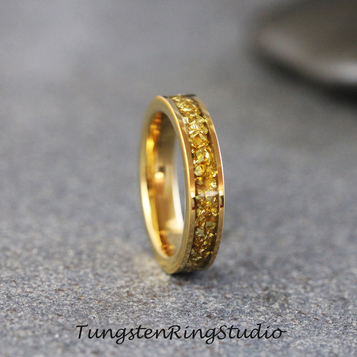 May include: A gold tungsten carbide ring with a band of yellow gold-colored particles.