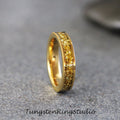 May include: A gold tungsten carbide ring with a band of yellow gold-colored particles.