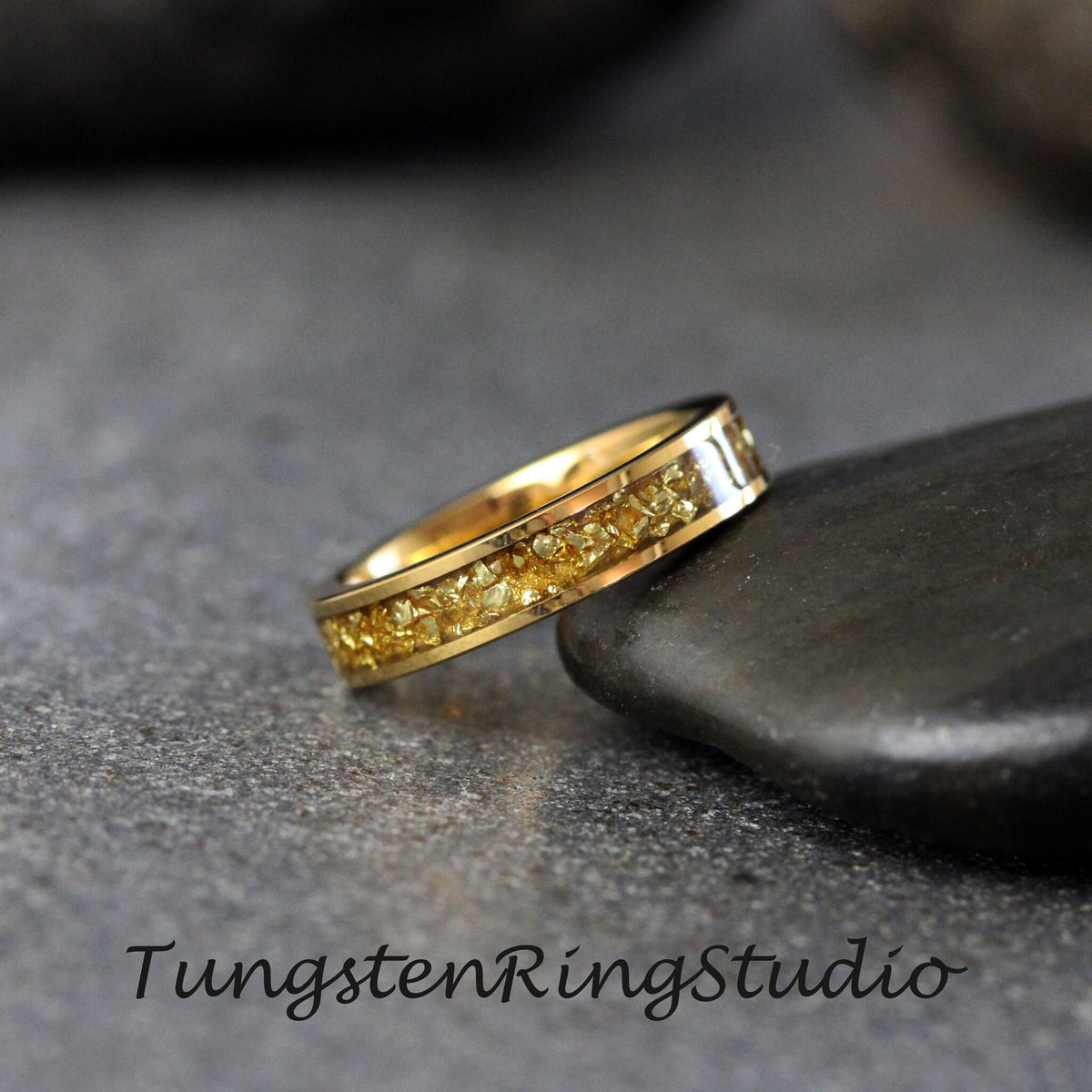 May include: A gold tungsten ring with a band of embedded gold nuggets. The ring is on a gray stone surface.