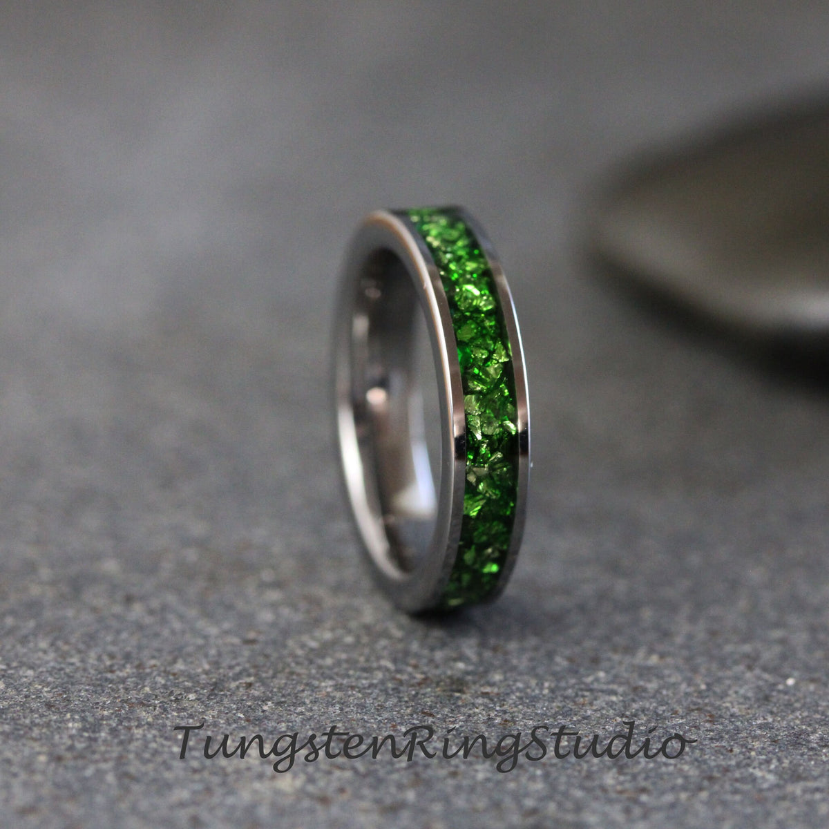 May include: A silver tungsten ring with a green glitter band. The band is made of small green crystals that are embedded in the metal.