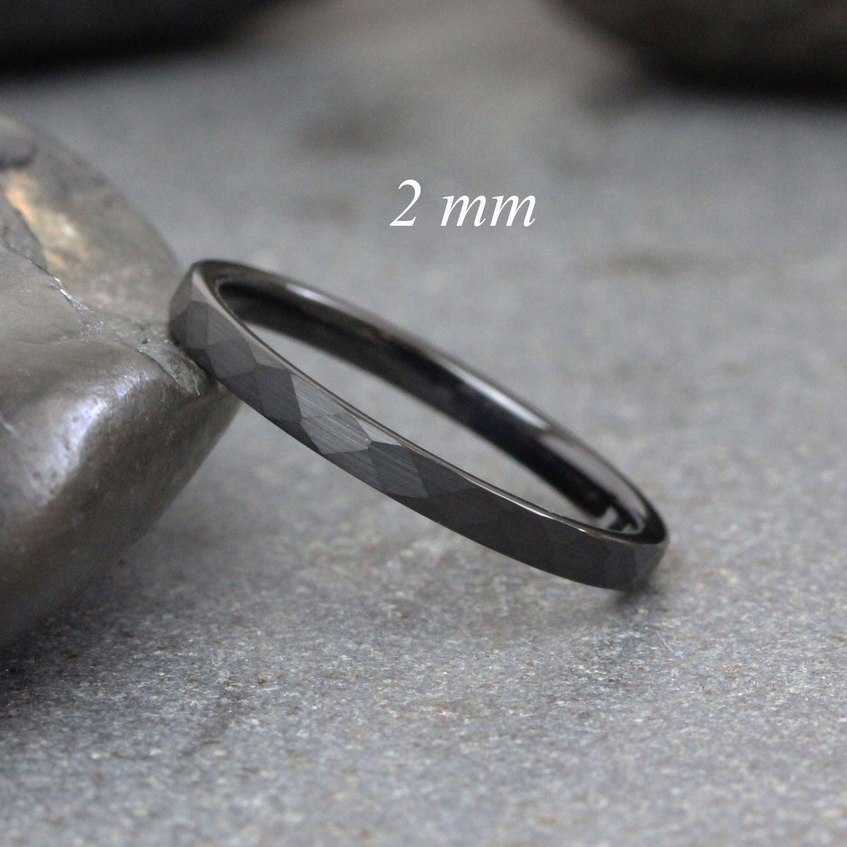 May include: A black, 2 mm wide,  faceted tungsten carbide ring. The ring is shown on a gray, textured surface.
