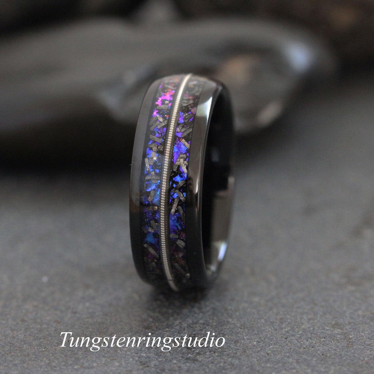 May include: A black tungsten carbide ring with a silver inlay and a blue and purple meteorite inlay. The ring is on a gray background.