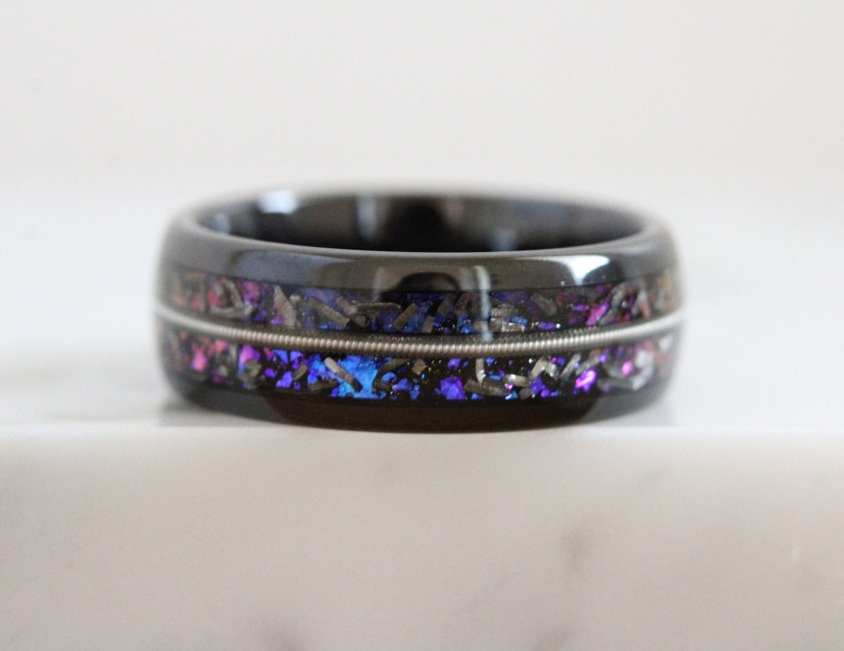 May include: A black ring with a silver band and a purple and blue inlay. The inlay is made of crushed meteorite and resin.