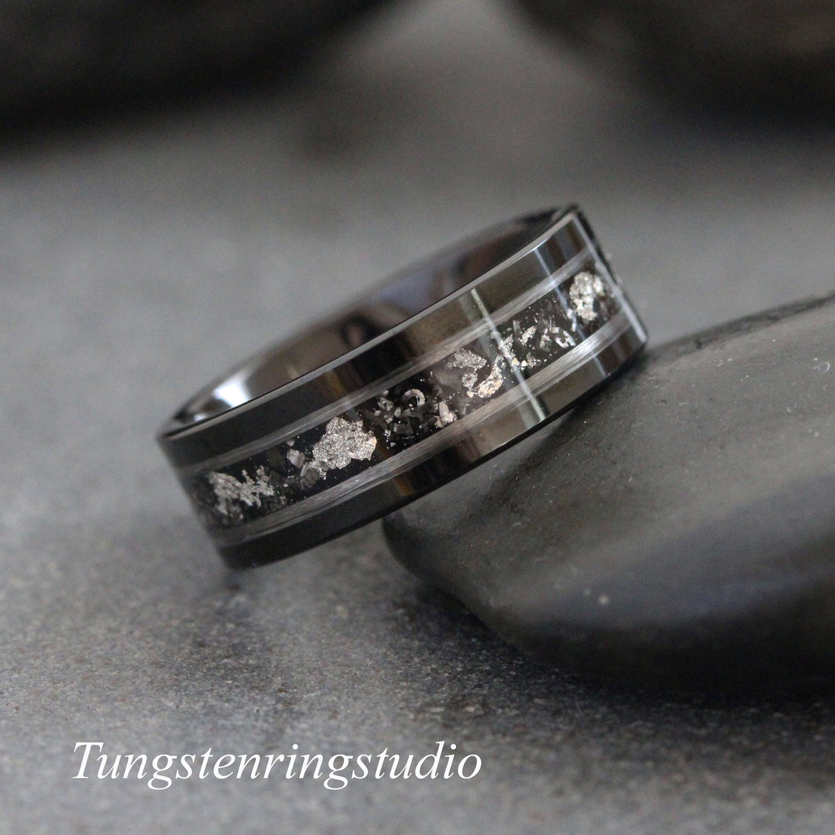 May include: A black tungsten carbide ring with a silver inlay. The inlay has a scattered pattern of small silver pieces.
