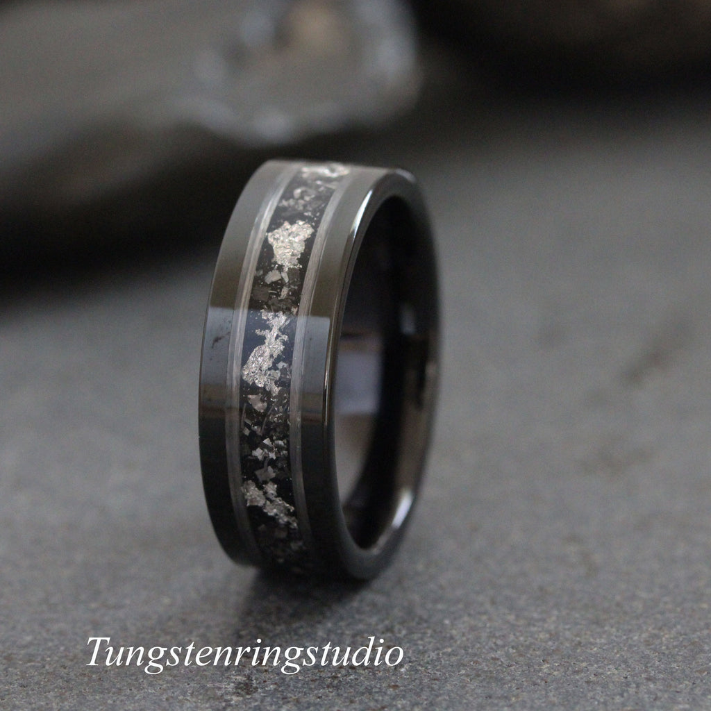 May include: A black tungsten carbide ring with a silver inlay. The inlay is a thin line of silver that runs around the band. The ring is polished and has a high shine.