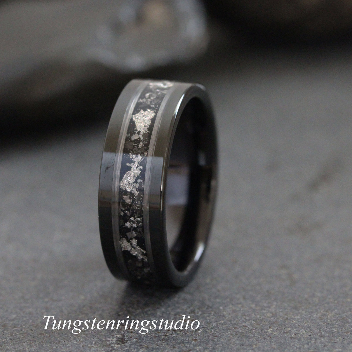May include: A black tungsten carbide ring with a silver inlay. The inlay is a thin line of silver that runs around the band. The ring is polished and has a high shine.