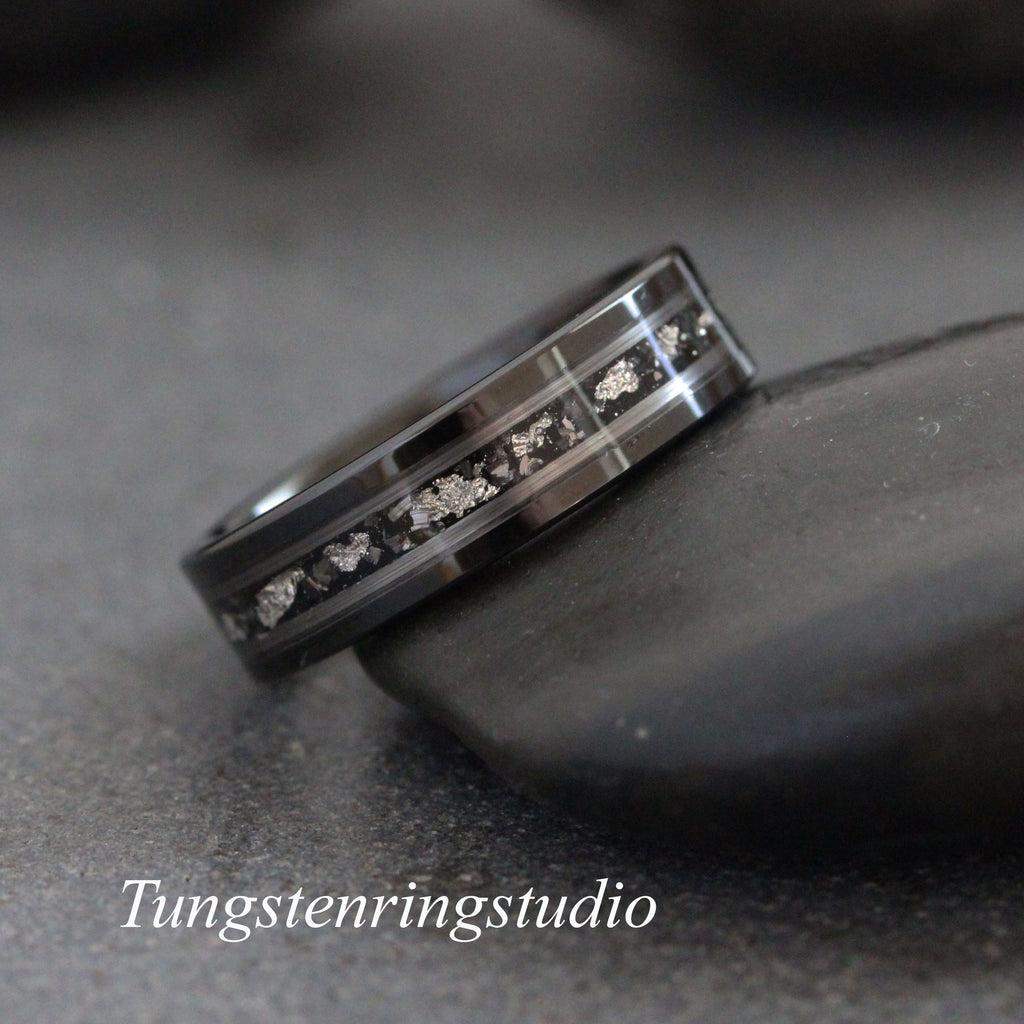 May include: A black tungsten carbide ring with a silver inlay. The inlay is a thin line of silver that runs around the band. The ring is on a gray background.