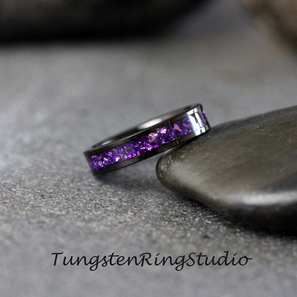 May include: A black tungsten ring with a band of purple gemstones. Tungsten Ring Studio.