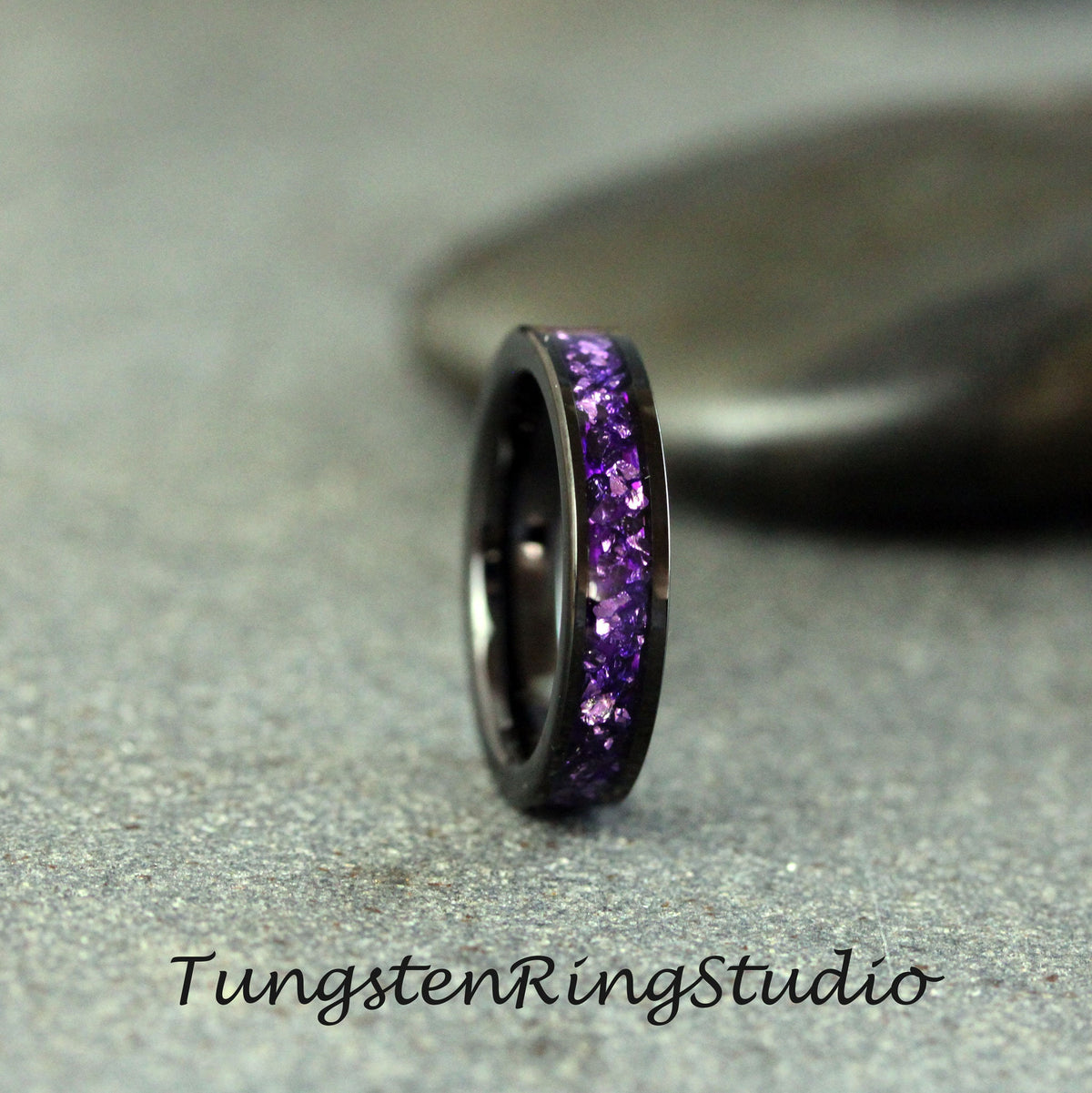 May include: A black tungsten ring with a band of purple glitter. Tungsten Rings Studio.