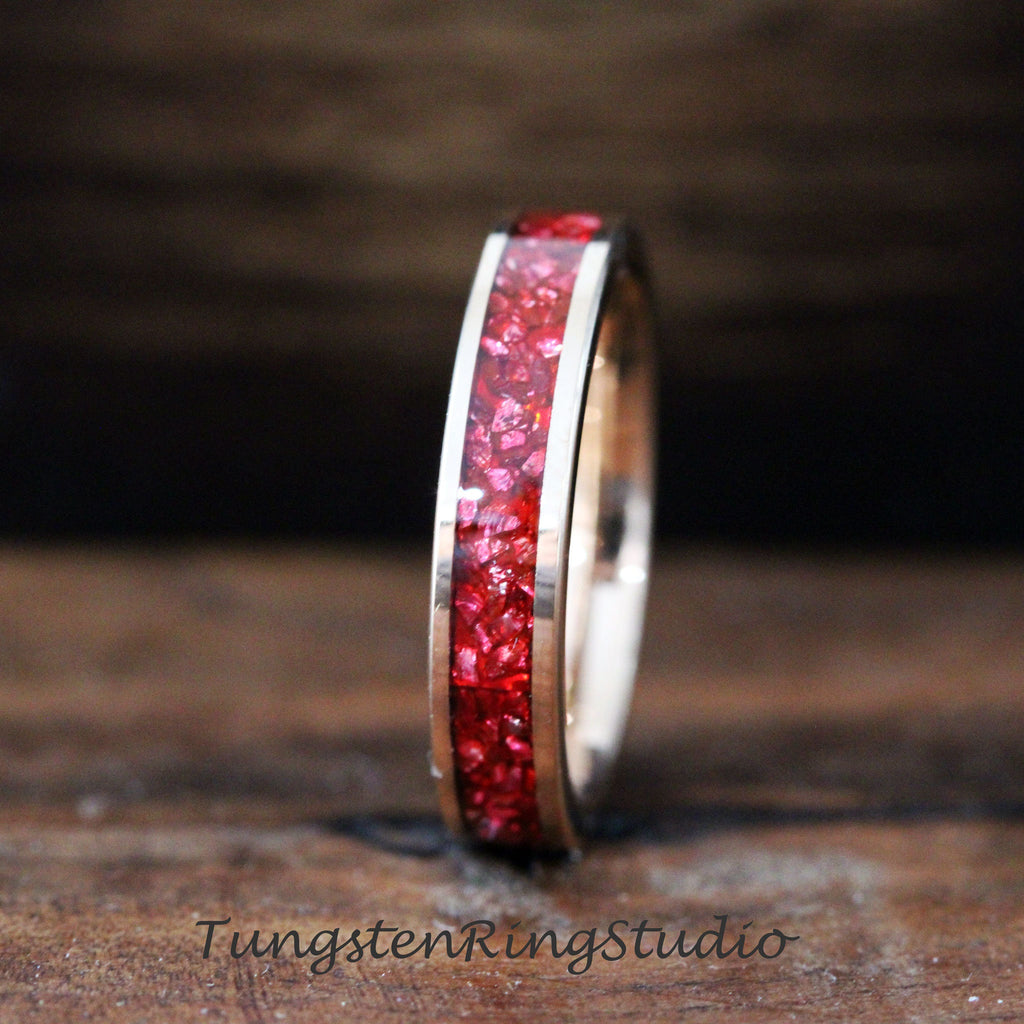 May include: A close-up of a silver tungsten ring with a red inlay. The inlay is made of small, red pieces of material that are set into the ring.
