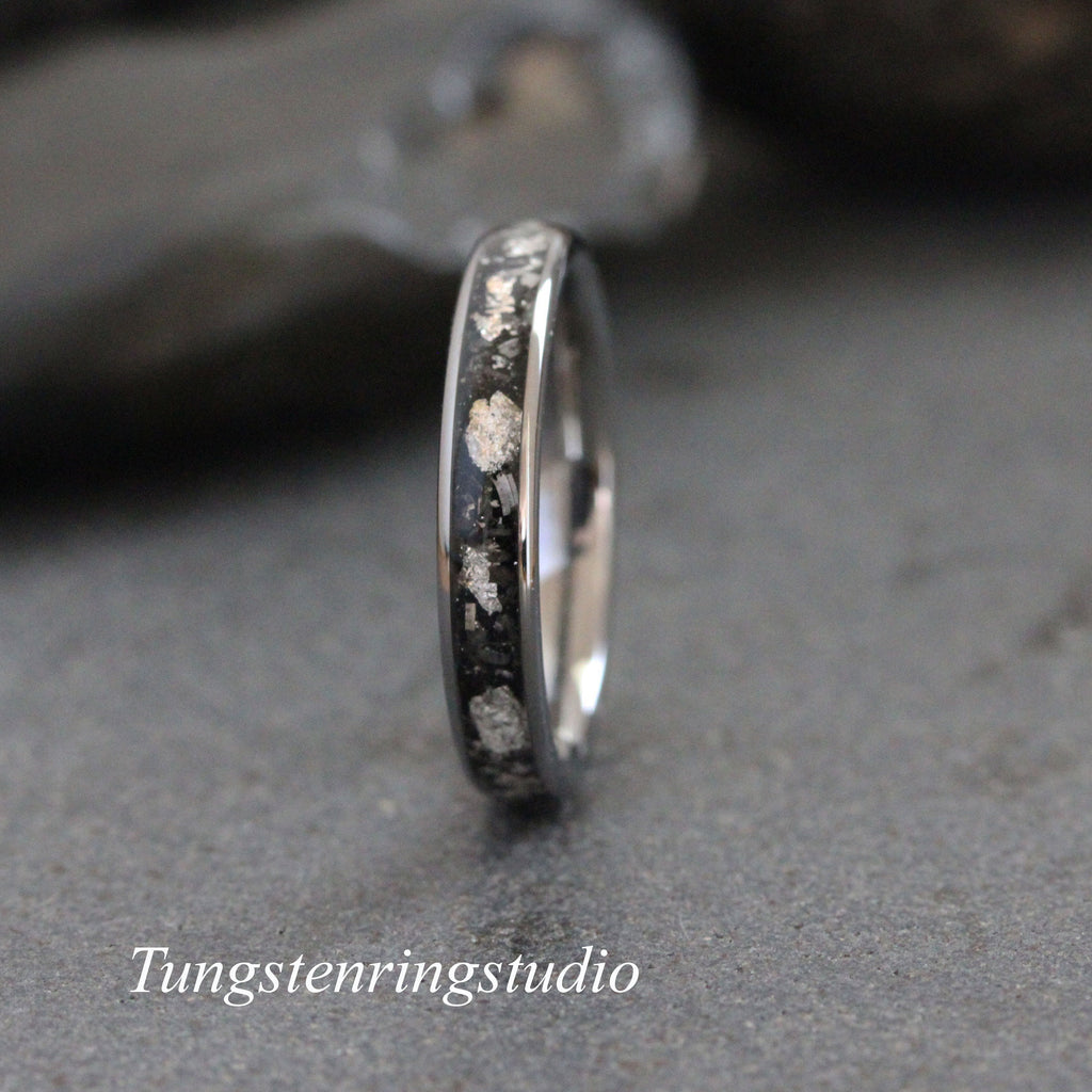 May include: A silver tungsten carbide ring with a black inlay and silver flecks. The ring is a simple band style.