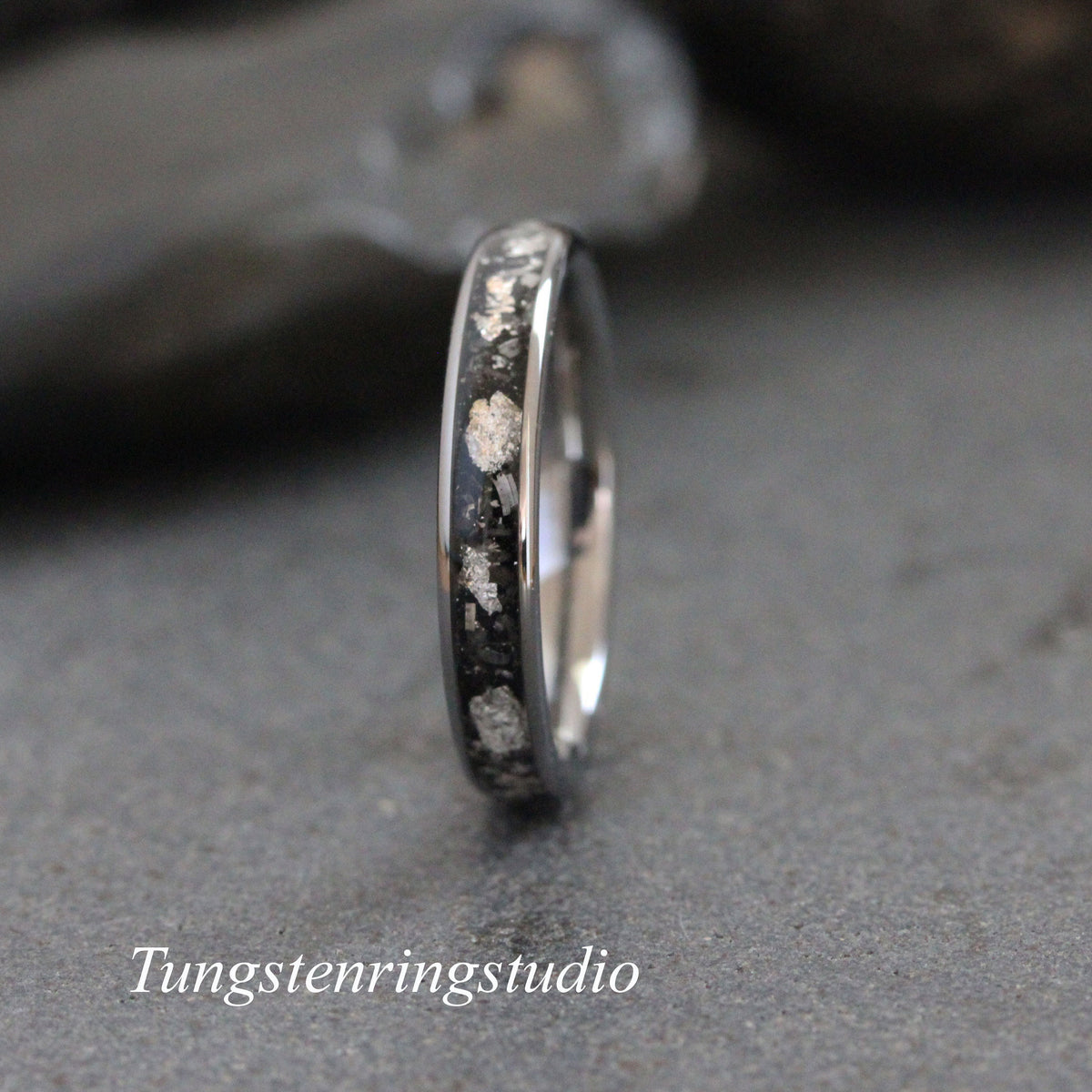 May include: A silver tungsten carbide ring with a black inlay and silver flecks. The ring is a simple band style.