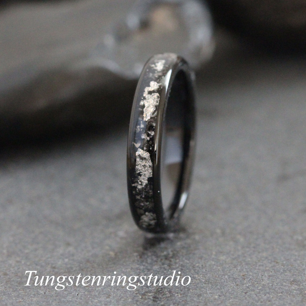 May include: A black tungsten carbide ring with a silver inlay. The inlay is in a scattered pattern. Tungstenringsstudio is printed below the ring.
