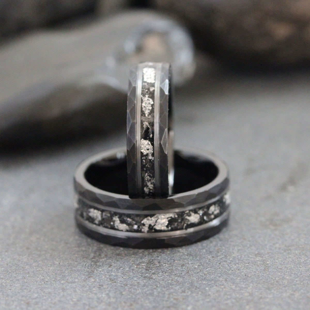 May include: Two black rings with a hammered finish and a silver inlay. The rings are stacked on top of each other.