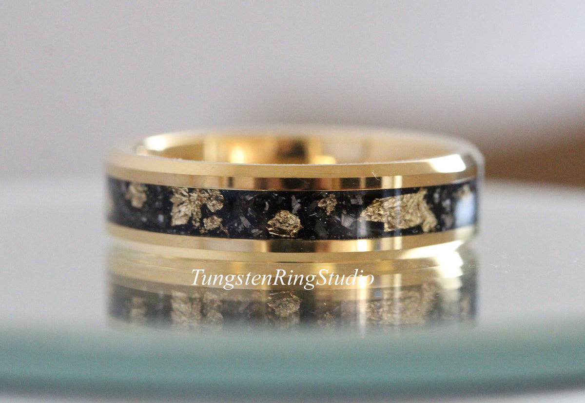 May include: A gold-colored ring with a black inlay featuring gold leaf accents. The ring has a polished finish and the text "TungstenRingStudio" is visible on the surface. This ring is a piece of jewelry.