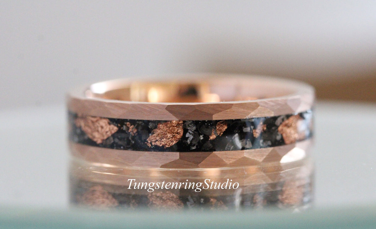 May include: A rose gold tungsten carbide ring with a black and copper inlay. The ring has a beveled edge and a textured surface.