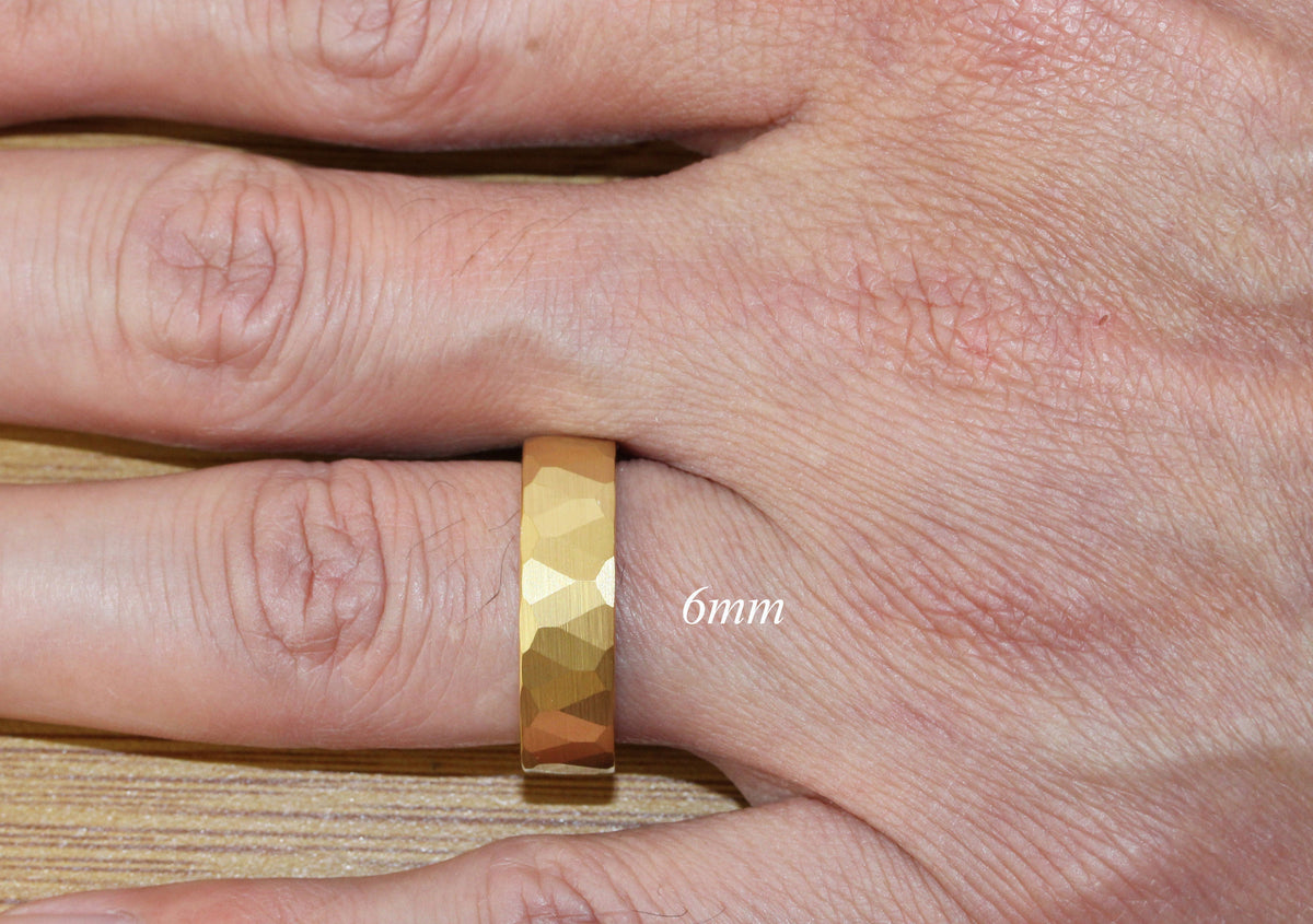 May include: A gold-colored ring with a hammered texture. The ring is 6mm wide and is worn on a person's finger.