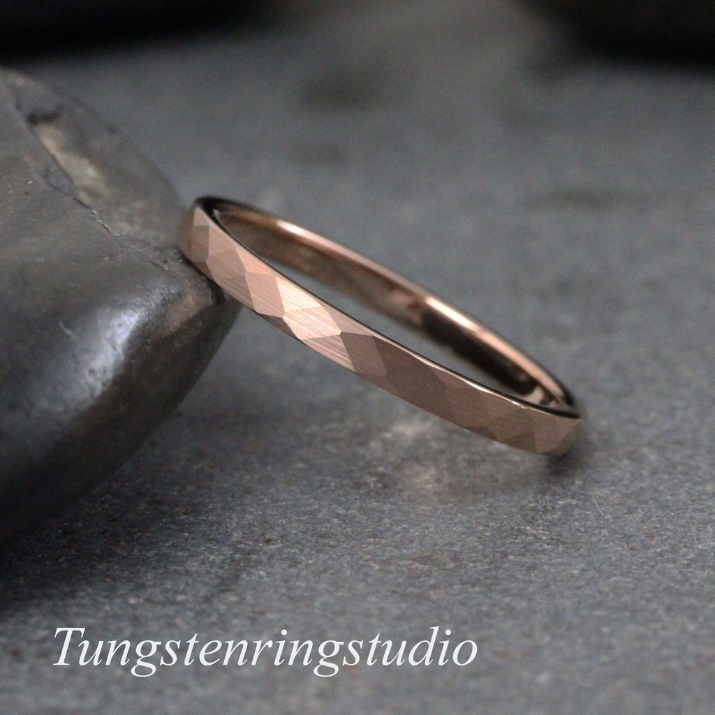 May include: A rose gold tungsten carbide ring with a hammered finish. The ring is thin and has a simple design.
