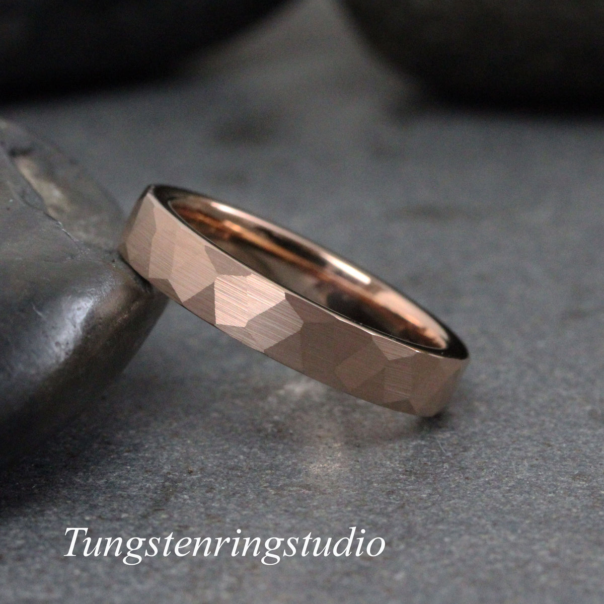 May include: A rose gold tungsten carbide ring with a hammered finish. The ring is a simple band with a slightly rounded edge.