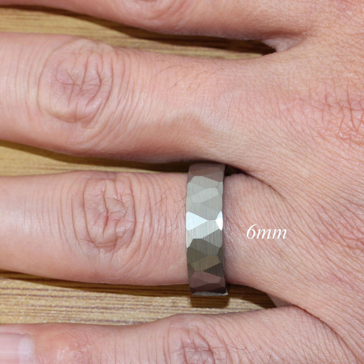 May include: A silver-toned hammered metal ring with a 6mm width. The ring is worn on a person's finger.