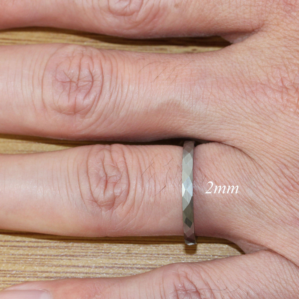 May include: A silver ring with a faceted design, worn on a finger. The ring is 2 mm wide.