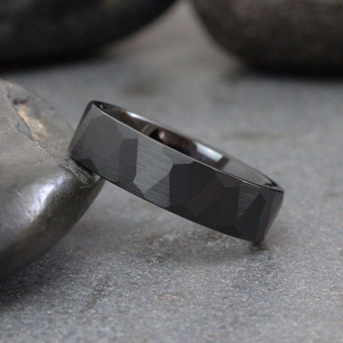 May include: A black, geometric patterned wedding band. The band has a matte finish and a slightly rounded edge.