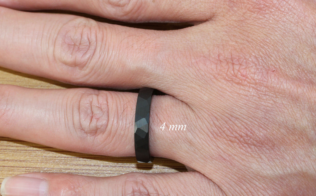 May include: A black ring with a faceted design, worn on a finger. The ring is 4 mm wide.